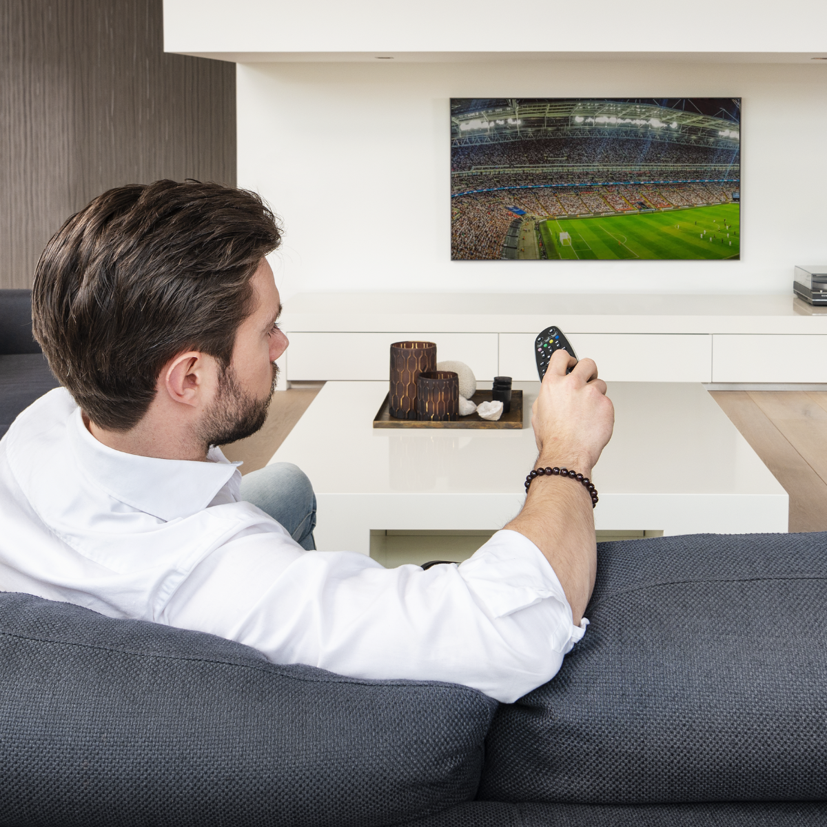 Invisible Control 6 XTRA - IR extender - man in from of tv with a remote control. AV equipment is in a closed closet | Marmitek