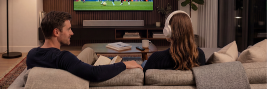 Man reading a book and woman watching football wearing headphones together on the sofa | Marmitek